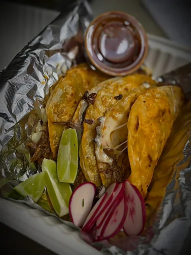 Quesabirria tacos in foil with a side of rich consomé and lime