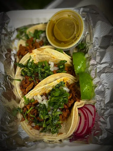 Al pastor tacos in a foil boat with green salsa and lime